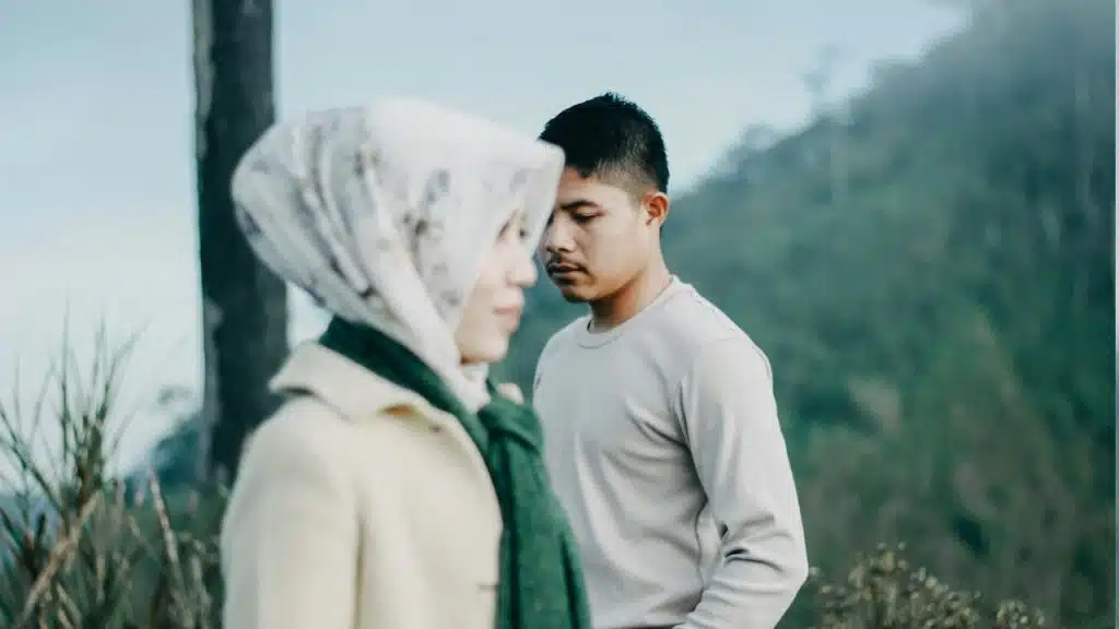 A man staring down while a woman wearing a scarf stands in the forefront.