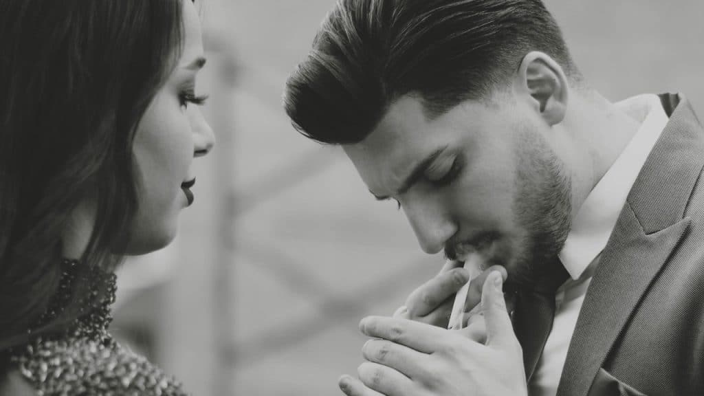 A woman looking at a man lighting a cigarette.