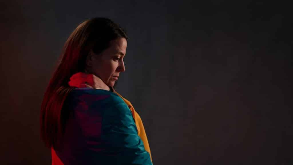 A woman looking downwards while standing in a dimly lit room with an intense expression.