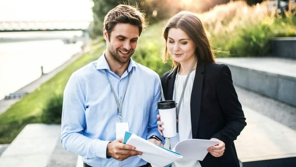 A man and a woman standing next to each other and reading a document.
