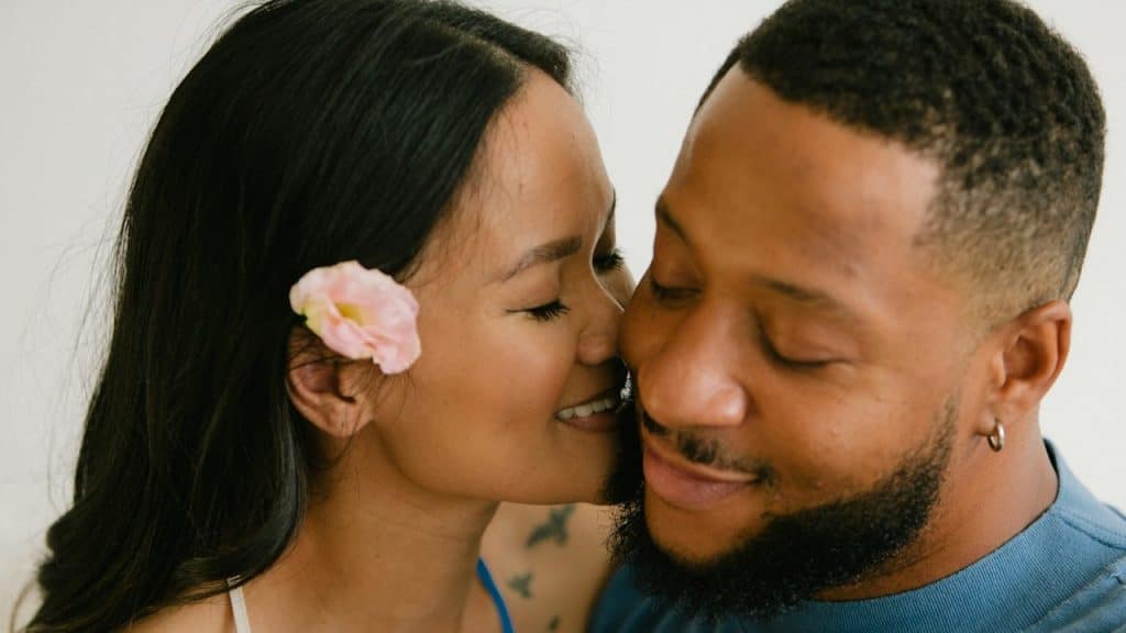 A woman smiling and about to kiss a bearded man’s cheek.