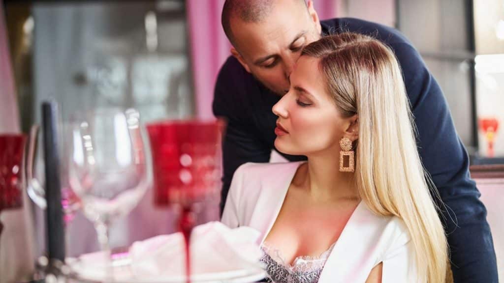 A guy planting a tender kiss on the face of a glamorous woman in a restaurant.