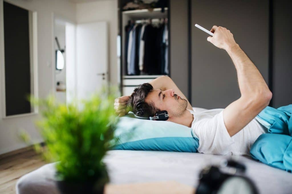 A man laying in bed while using a phone