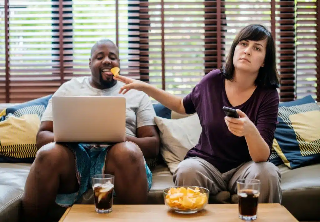 A woman watching a tv and a man using a laptop