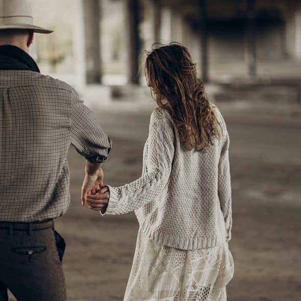 A man wearing a har about to hold a woman’s outstretched hand as they walk on a path.