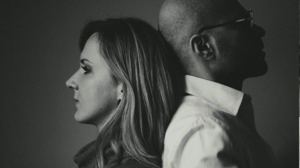 An upset couple standing with their backs touching.