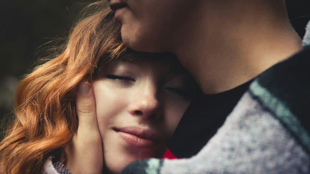 A person gently cups the face of a smiling woman with closed eyes and red hair.