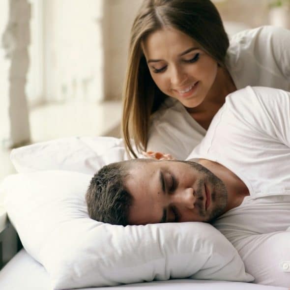 A woman and watching a man sleep while they lie on a bed.