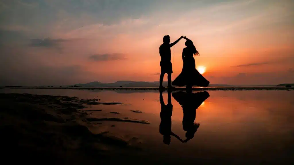 Silhouette of a man and woman dancing on a beach during sunset.