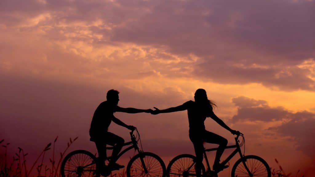 A woman on a bike reaching for a man's hand behind her, also on a bike.