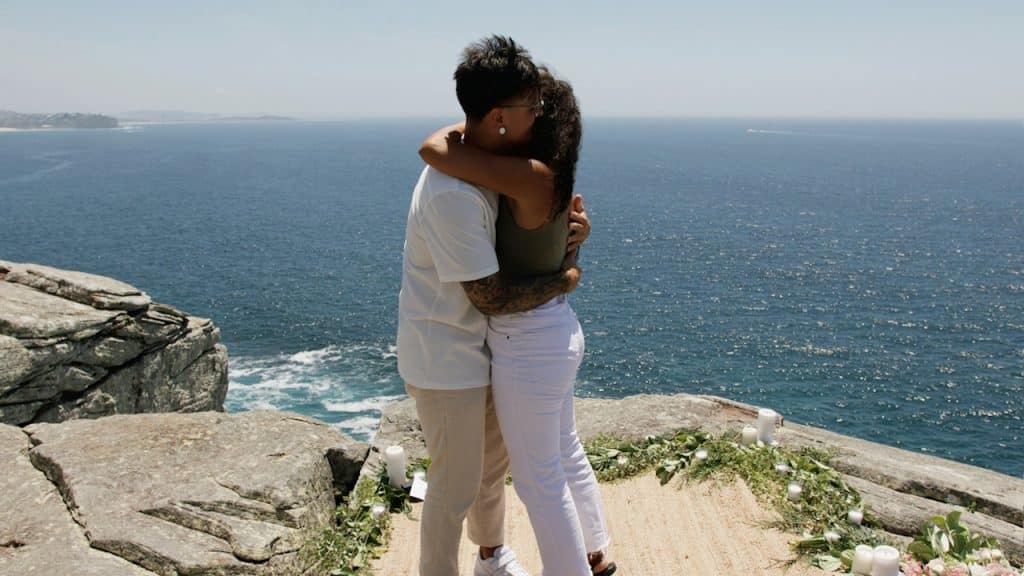 A man and a woman embracing on a cliff overlooking the ocean.