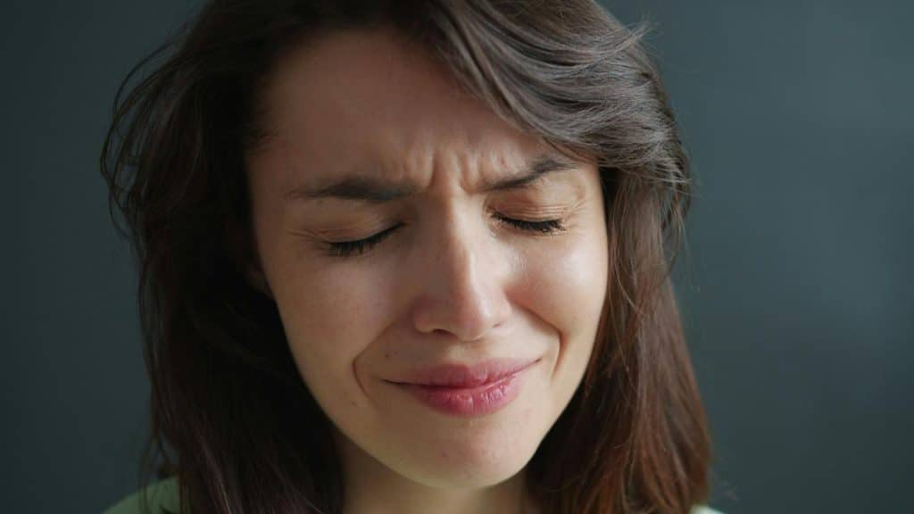 A woman with closed eyes and a pained, emotional expression.