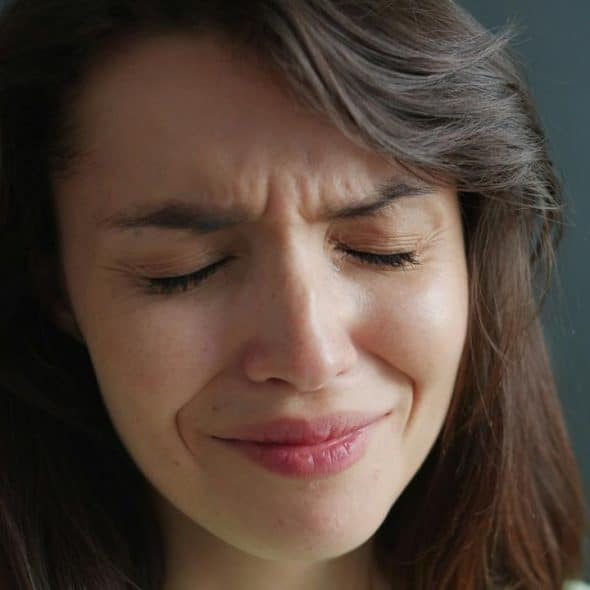 A woman with closed eyes and a pained, emotional expression.