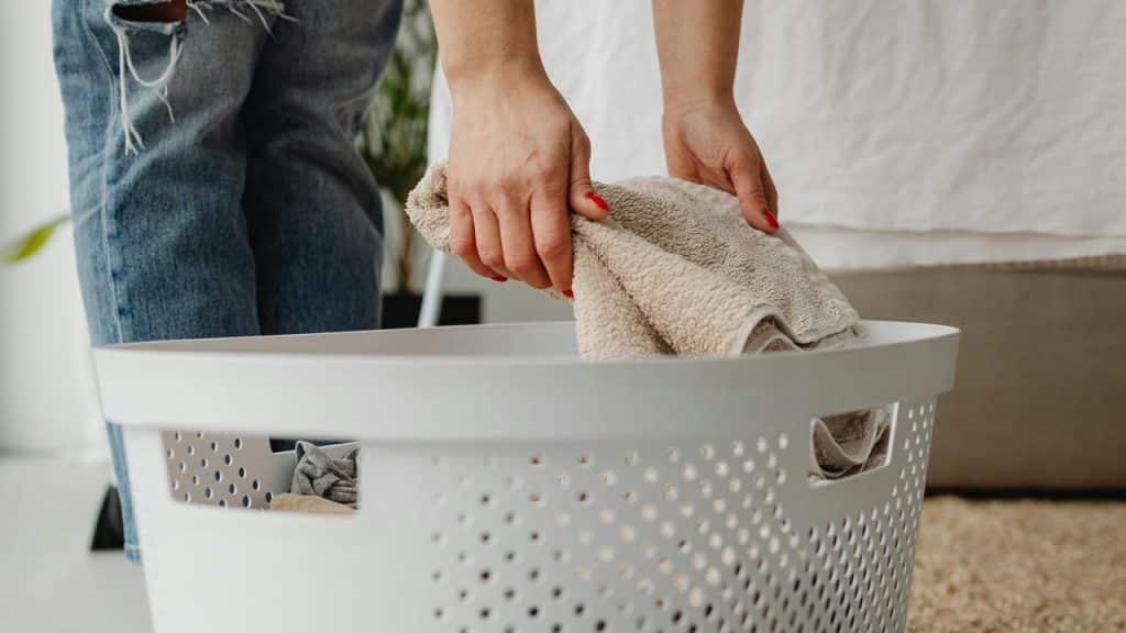 A person placing folded towels into a white laundry basket.