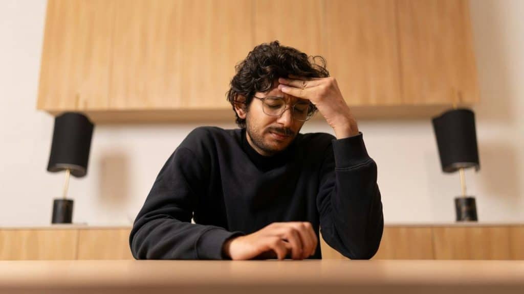A man sitting at a table with his hand on his forehead, looking stressed.