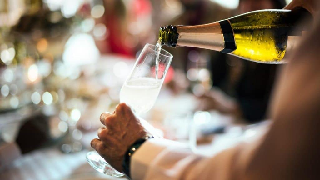 A waiter pouring sparkling wine into a champagne flute at a lively restaurant table.