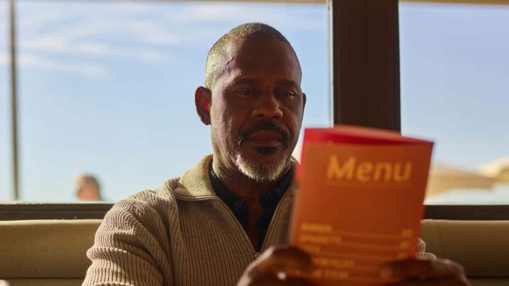 A man reading a restaurant menu while sitting by a window.