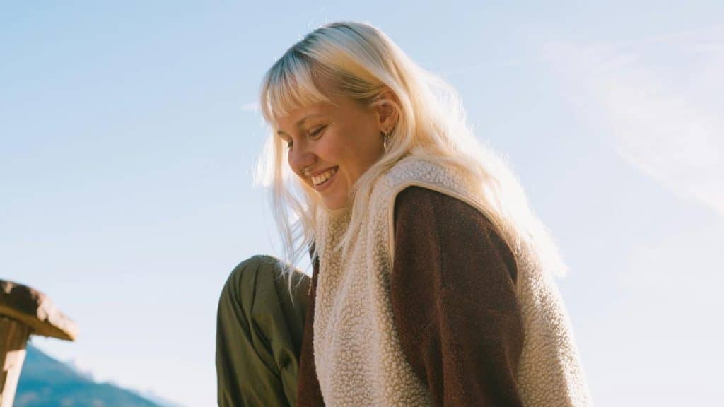 A smiling woman with light hair enjoying a sunny outdoor moment.