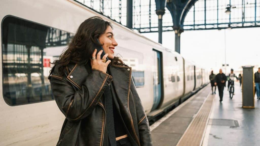 A woman smiling while talking on a phone at a train station platform.