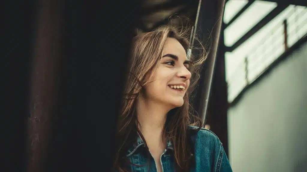 A young woman smiling outdoors near an industrial structure.