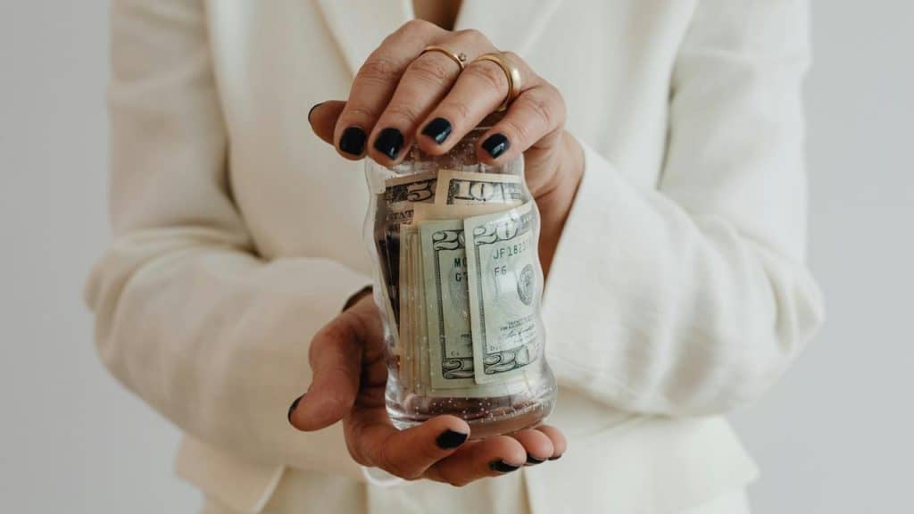 A person holding a glass jar filled with folded cash.