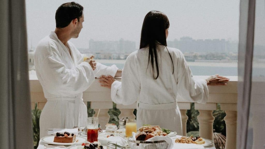 A couple in bathrobes on a balcony overlooking the water.