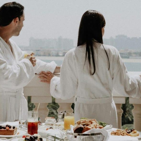 A couple in bathrobes on a balcony overlooking the water.