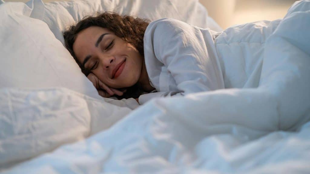 A woman sleeping peacefully in a bed with white sheets.