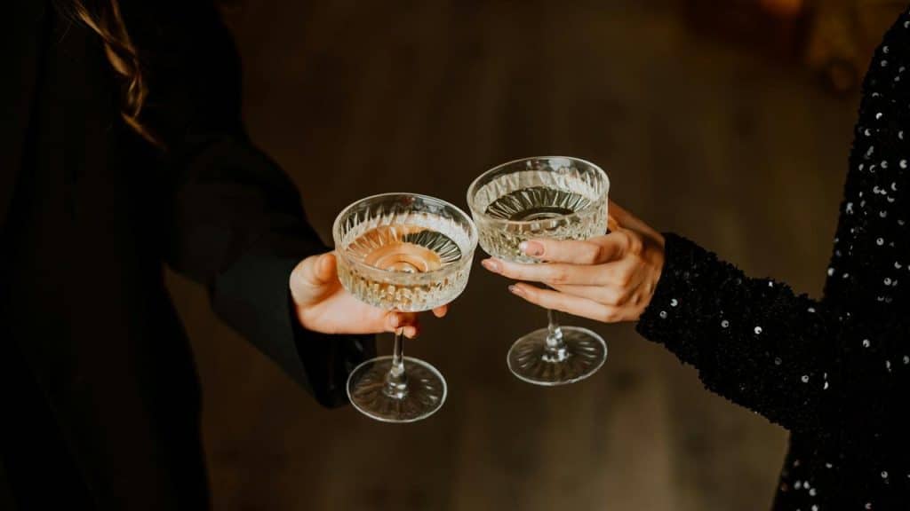 A close-up of two people clinking coupe glasses in a toast.