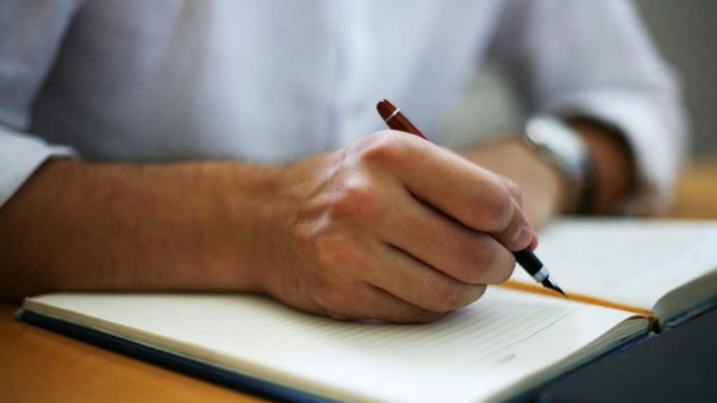 A close-up of a hand writing in a lined notebook with a pen.