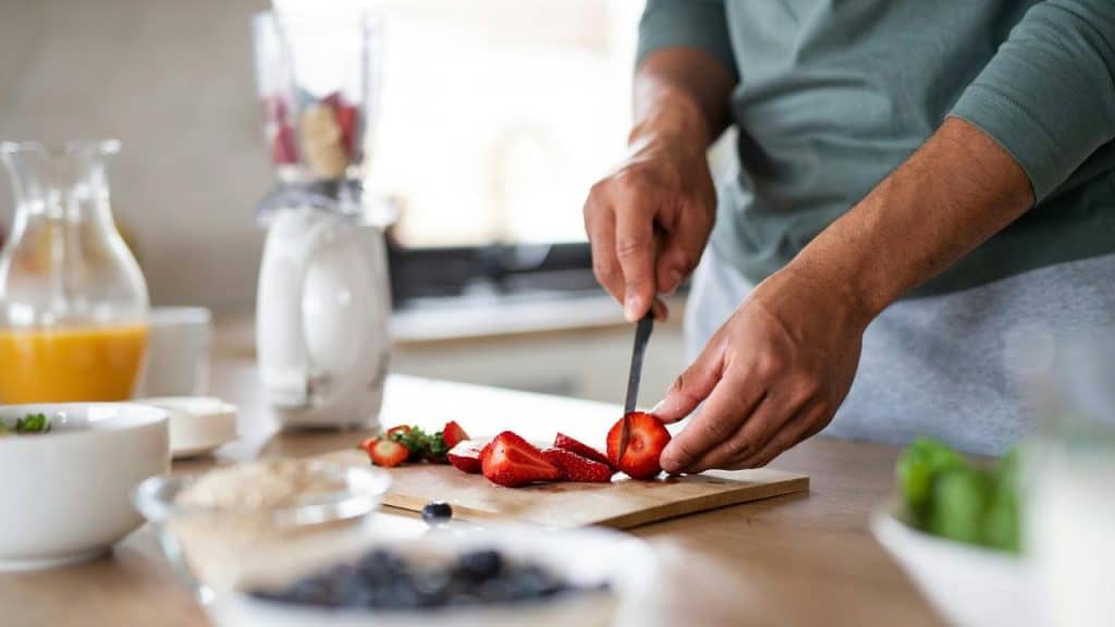 A person slicing fresh strawberries on a cutting board in a kitchen.