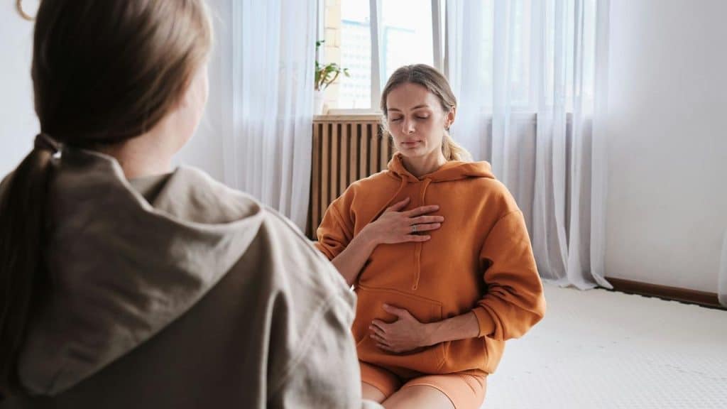 A woman practicing mindful breathing with her hand on her chest while seated indoors.