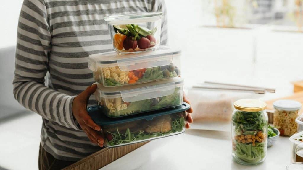 A person holding several stacked containers filled with prepared meals in a kitchen.
