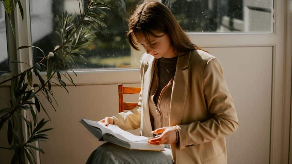 A woman reading a book by a sunlit window.