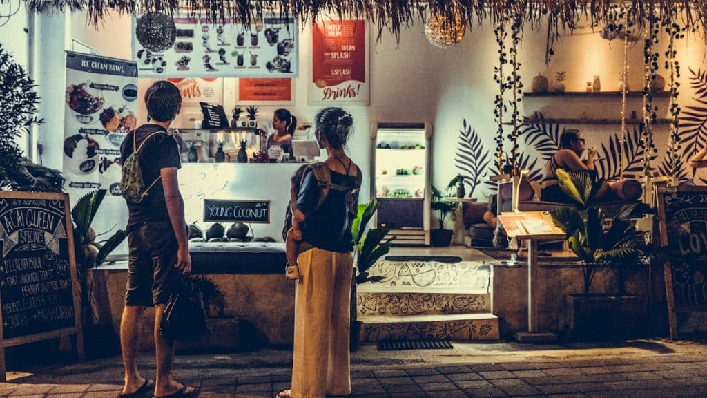 A woman carrying a baby standing in front of a store.