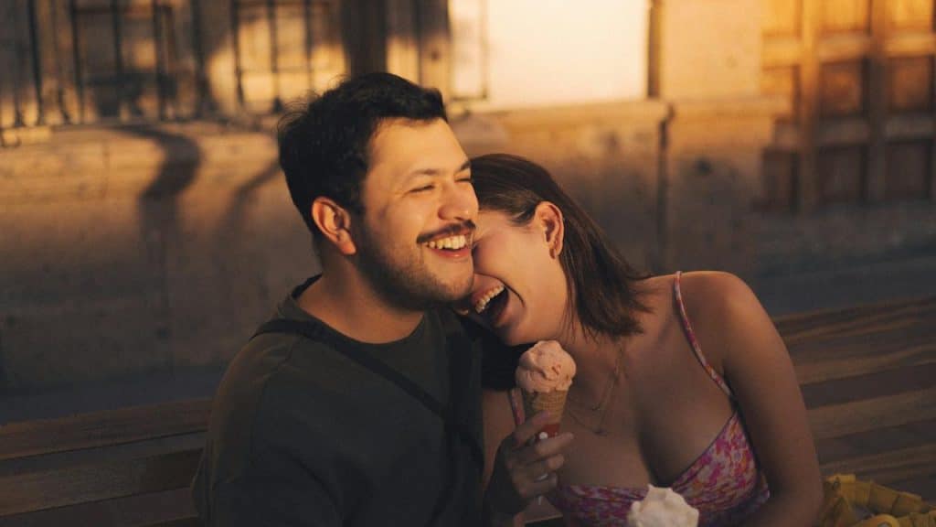 Happy man and woman sitting together, laughing, with the woman holding an ice cream cone.