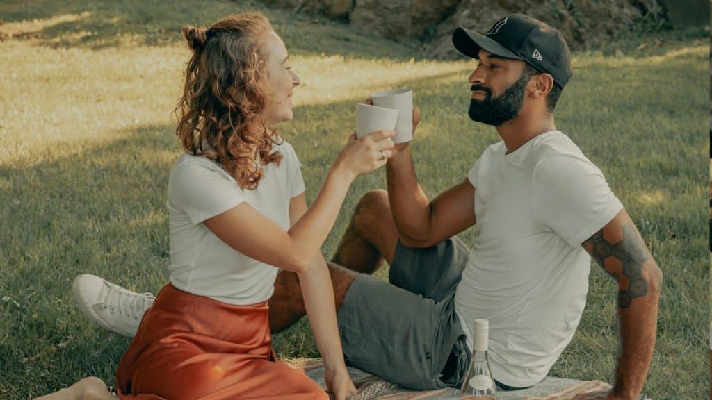 A man and a woman having tea while sitting on the grass.