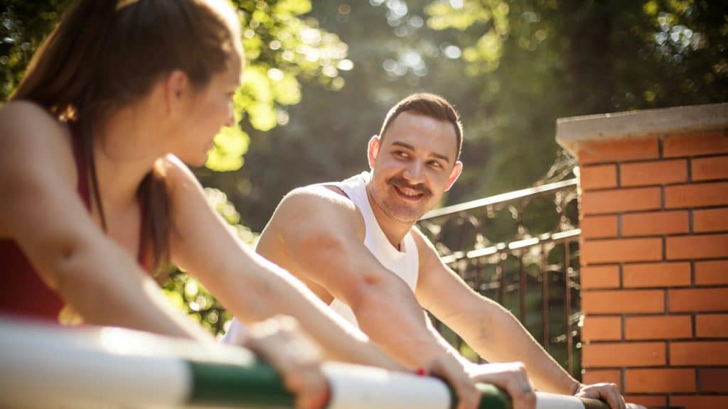 A man and a woman smiling during a workout at daytime.
