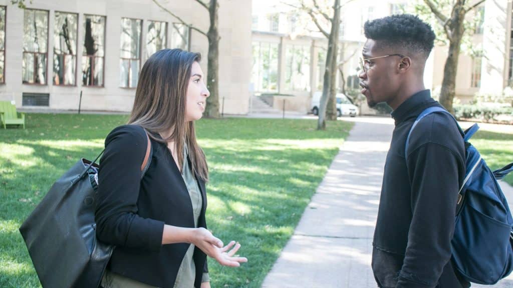 A man and a woman talking to each other while standing on a footpath.