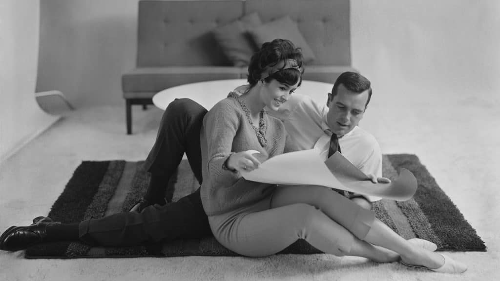 A man and a woman looking at a rolled paper while sitting on the floor.