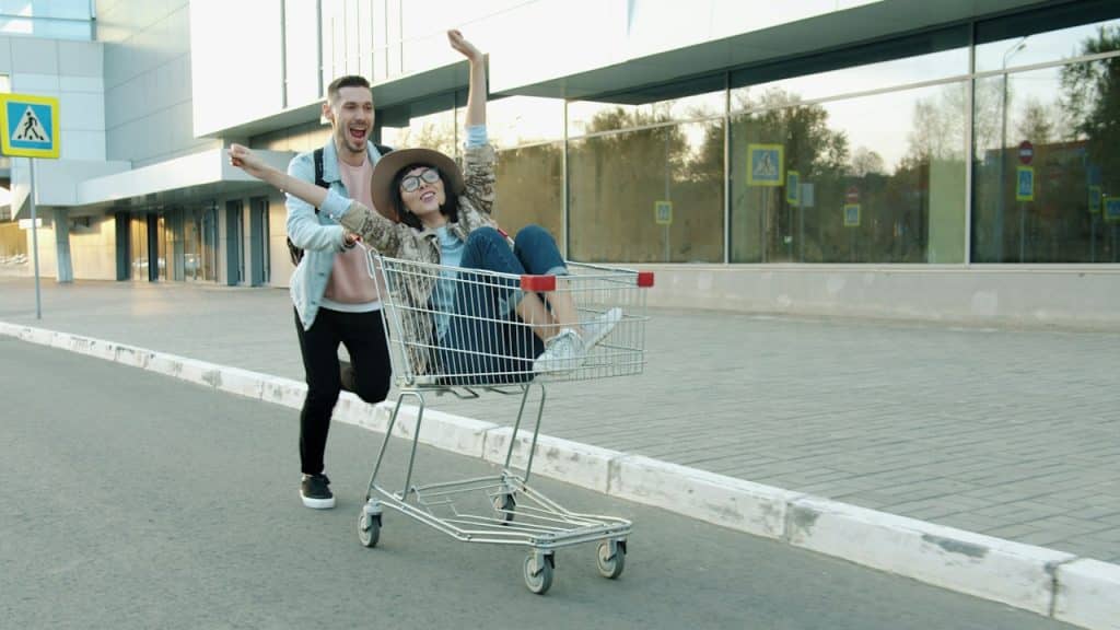 A couple having fun riding in a shopping cart.