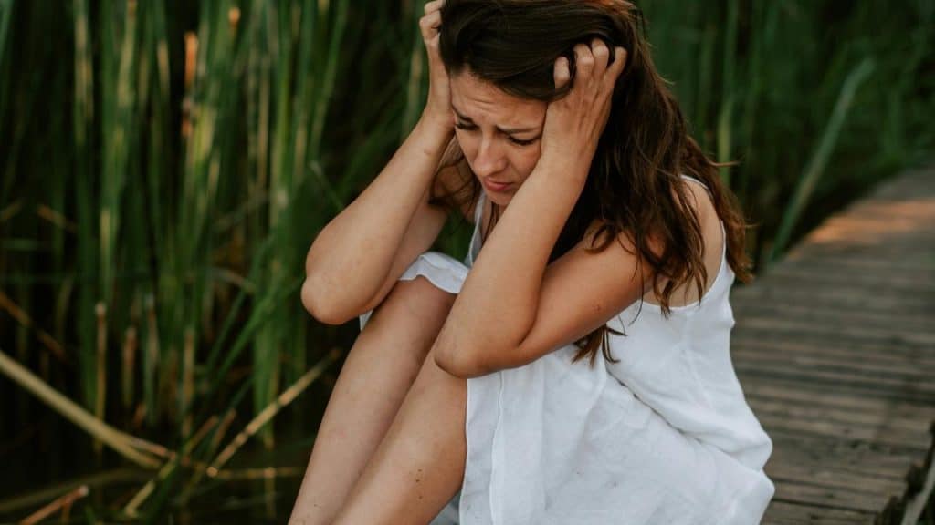 A distressed woman sitting on a wooden dock holding her head.