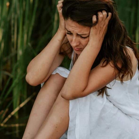 A distressed woman sitting on a wooden dock holding her head.