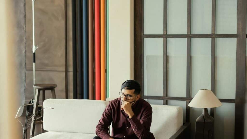 A man sitting thoughtfully on a couch in a studio setting with colorful backdrops
