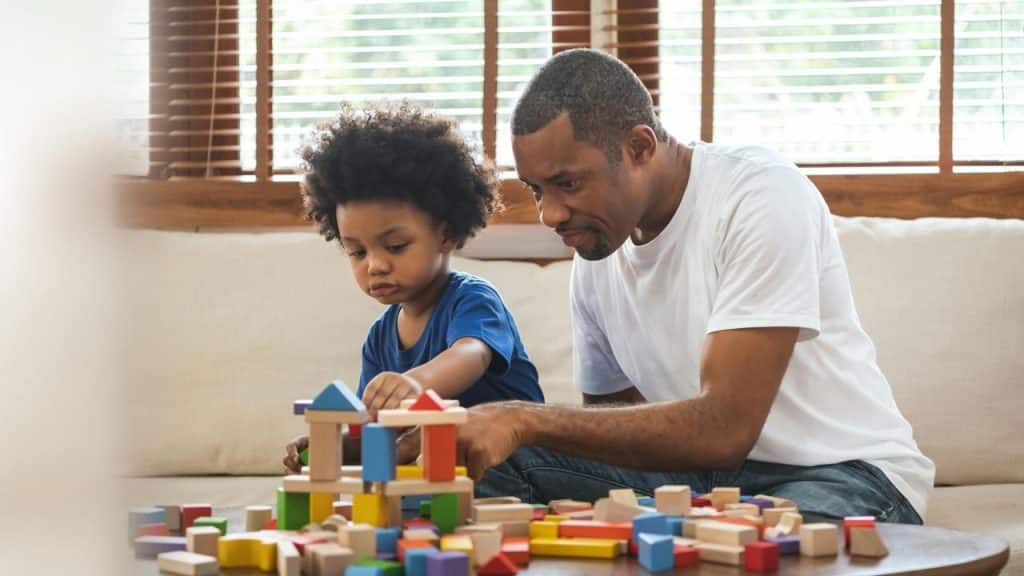 A father and young child playing with colorful wooden blocks on a table.