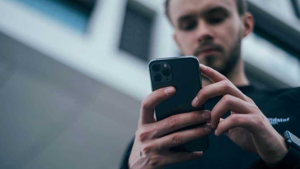 A man using a smartphone outdoors with a blurred building in the background.