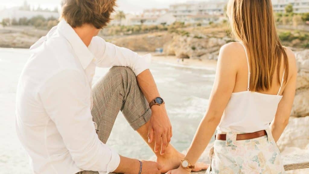 A couple sitting by the seaside, looking out over the water.