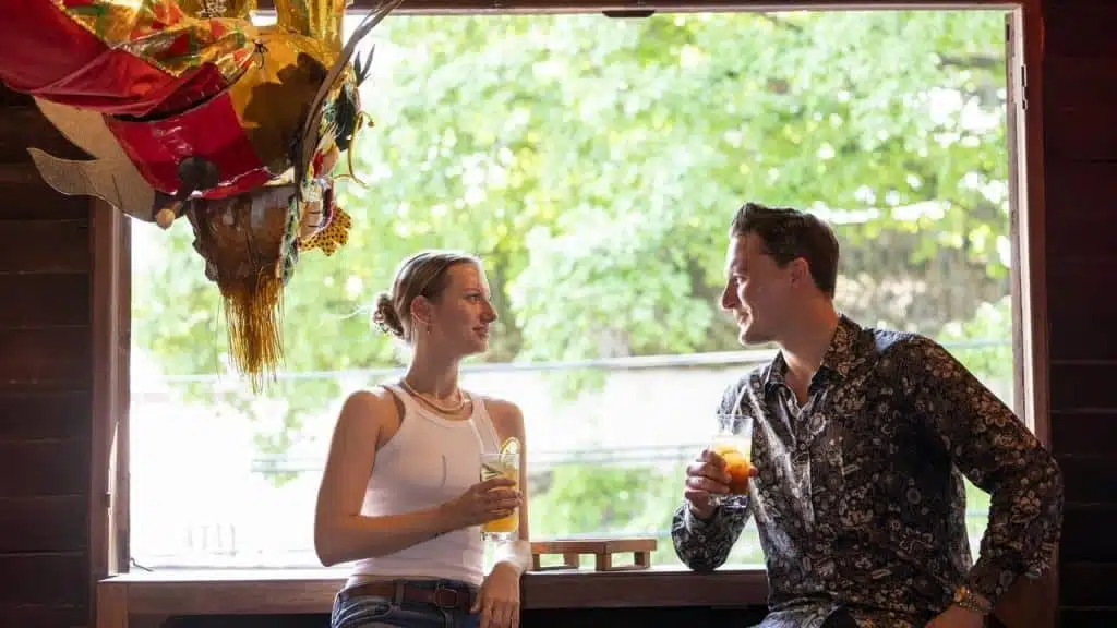 A couple chatting and holding drinks by an open window.