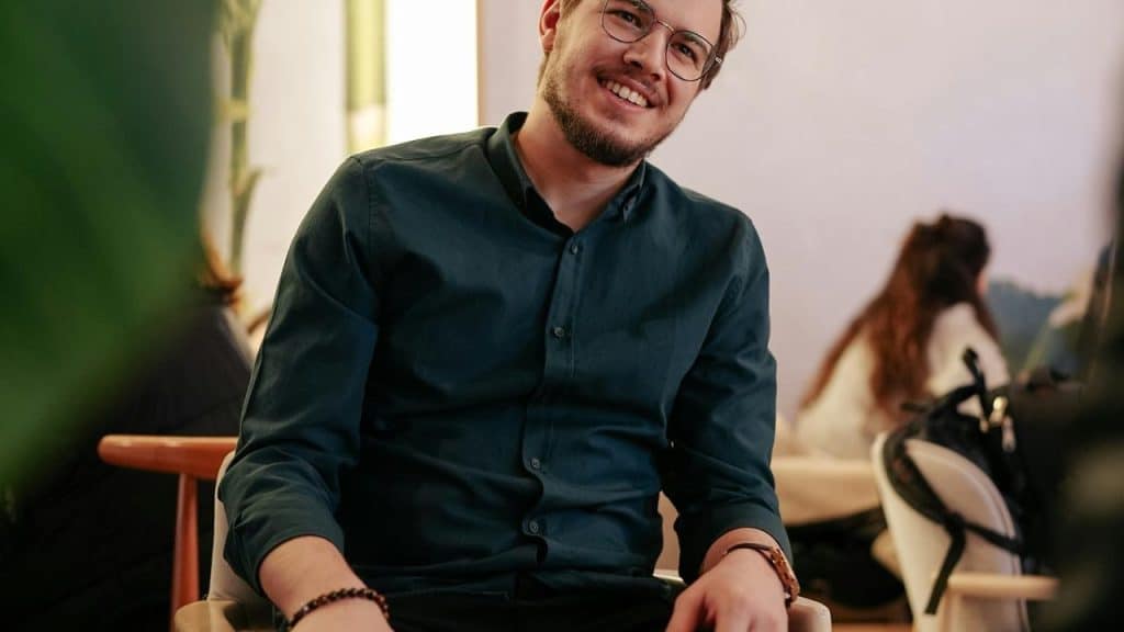 A smiling man wearing glasses sitting indoors at a café.
