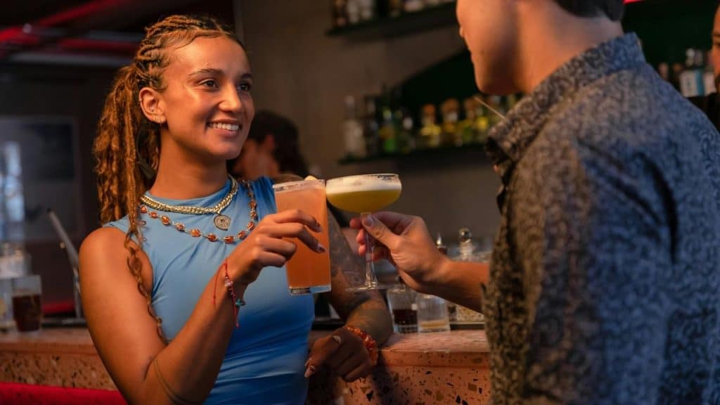 A woman smiling and clinking drinks with a companion at a bar.